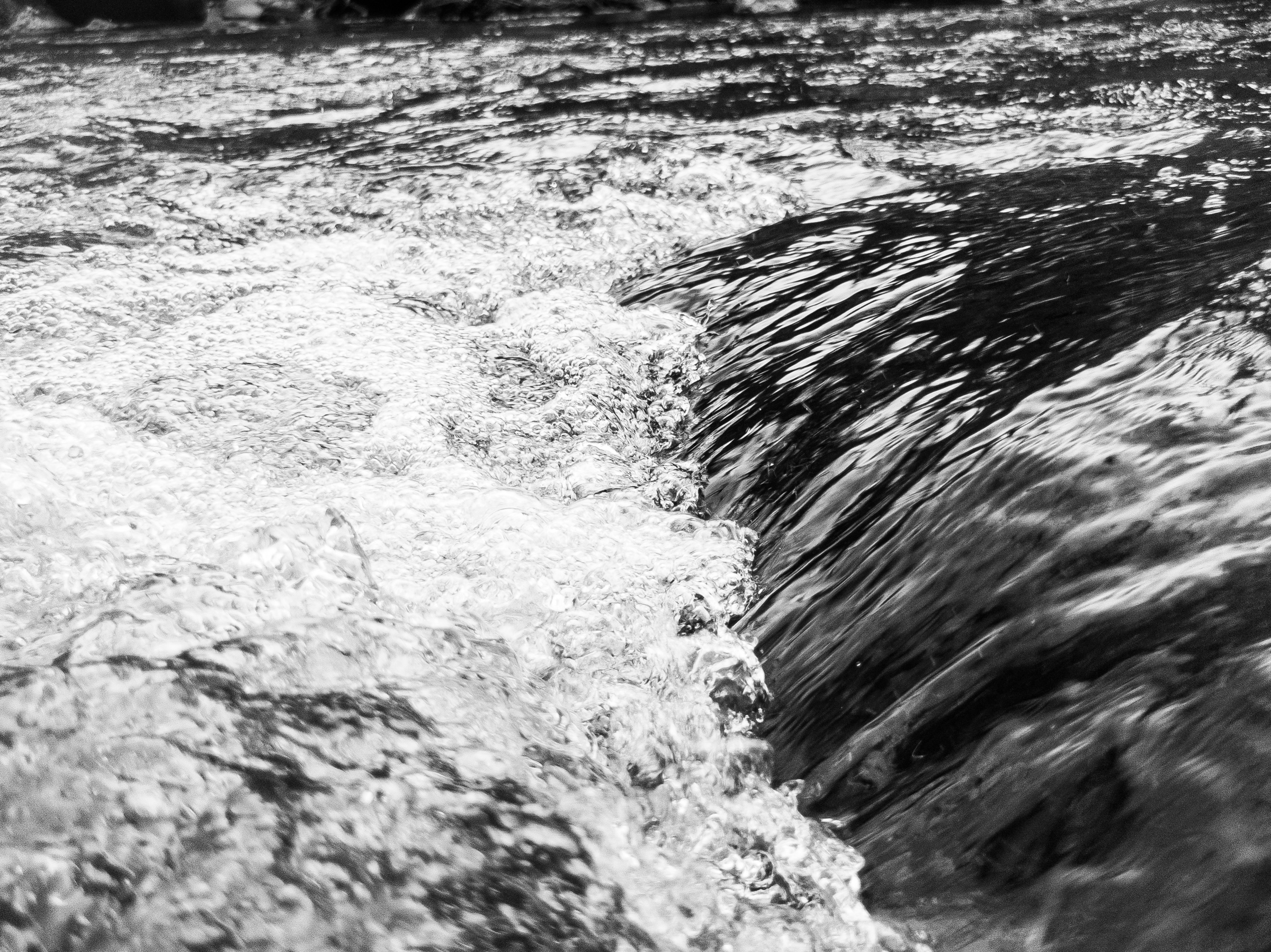 A close-up picture of a some froth on a tiny wave in black-and-white.