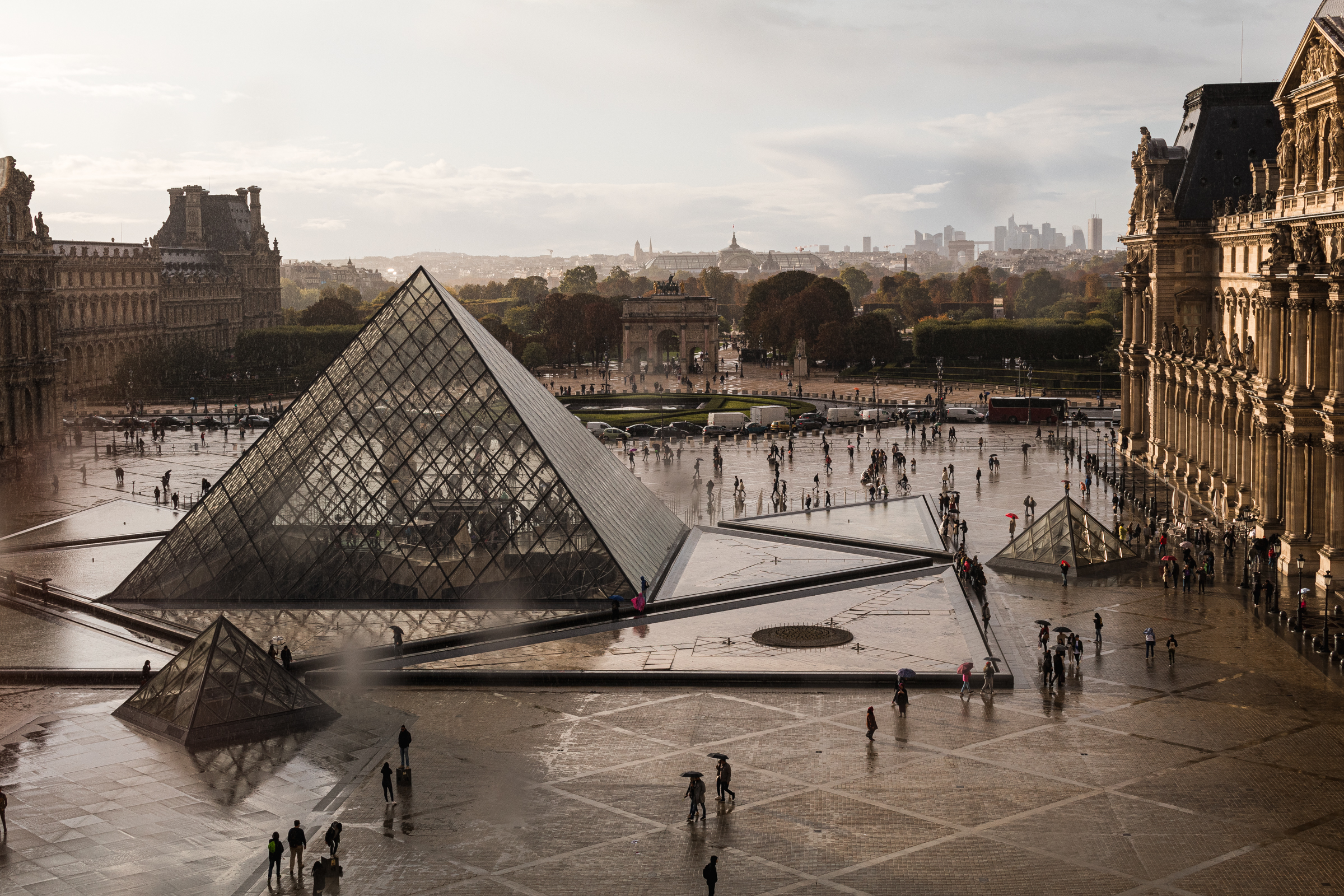 A wide shot of the Louvre's pyramid entrance, shot from the upper floors so you can see the square surrounding it.