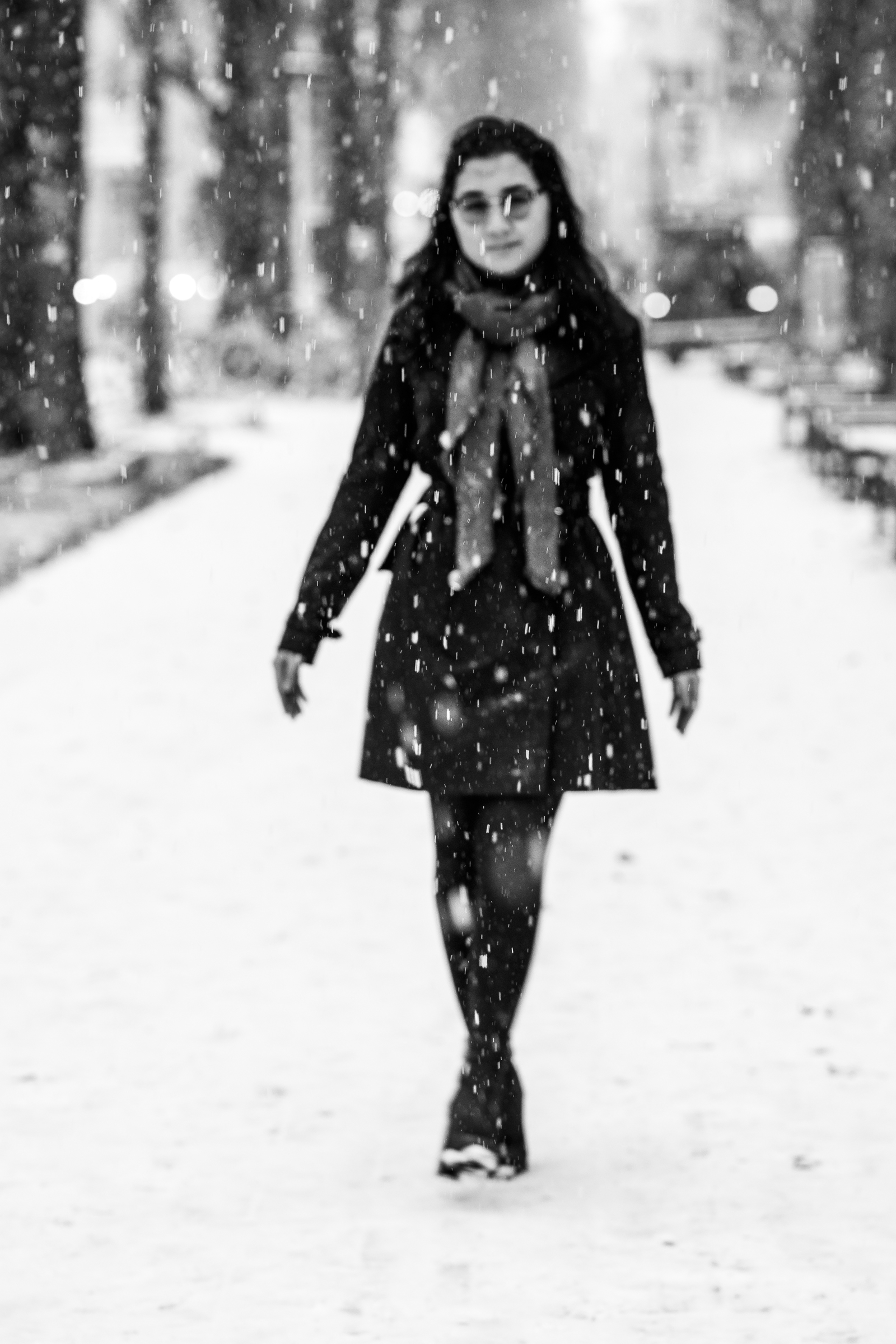 Black-and-white photo of a blurry woman standing with crossed legs amidst falling snow.