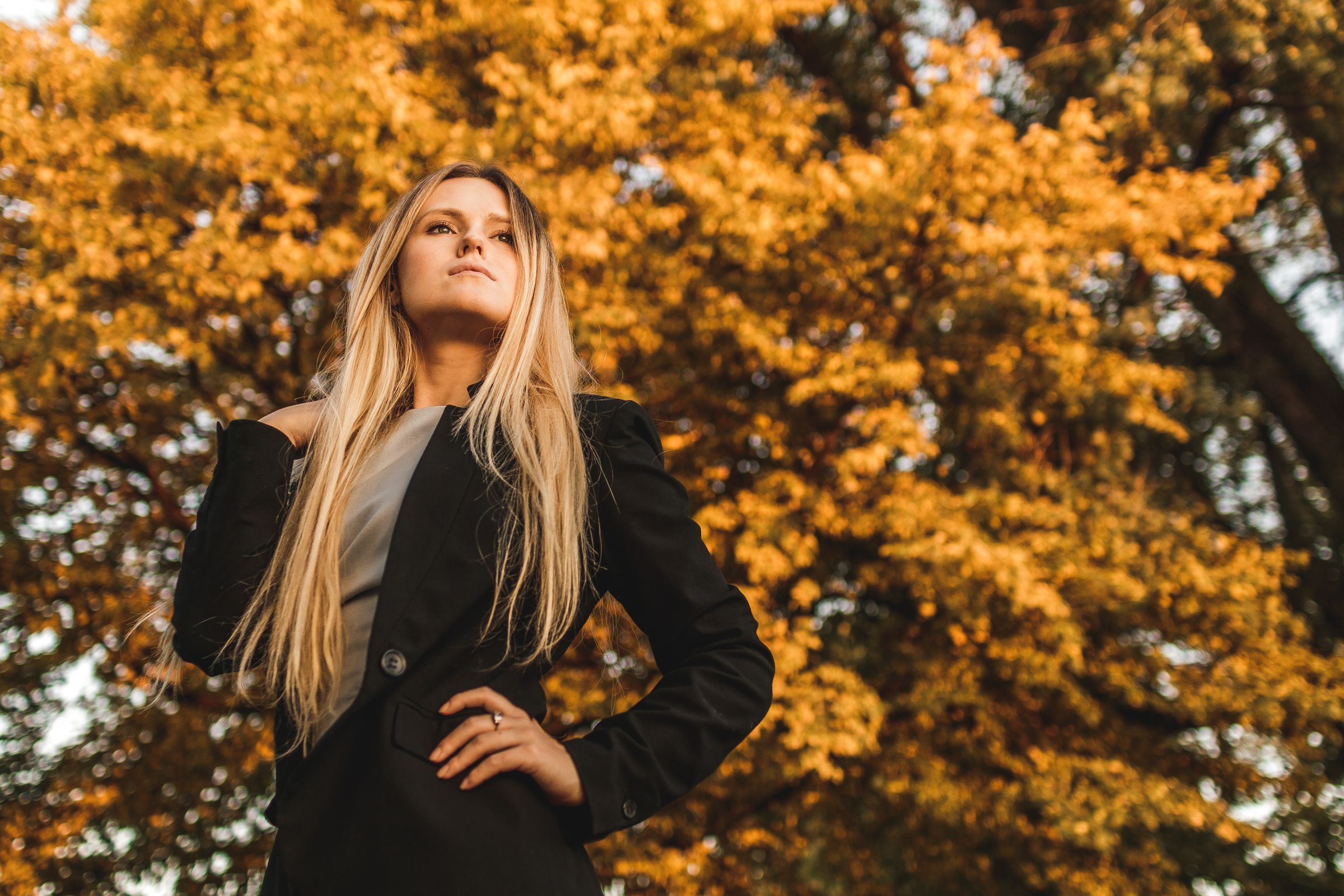 A blonde woman standing in front of a tree with yellow leaves in autumn.